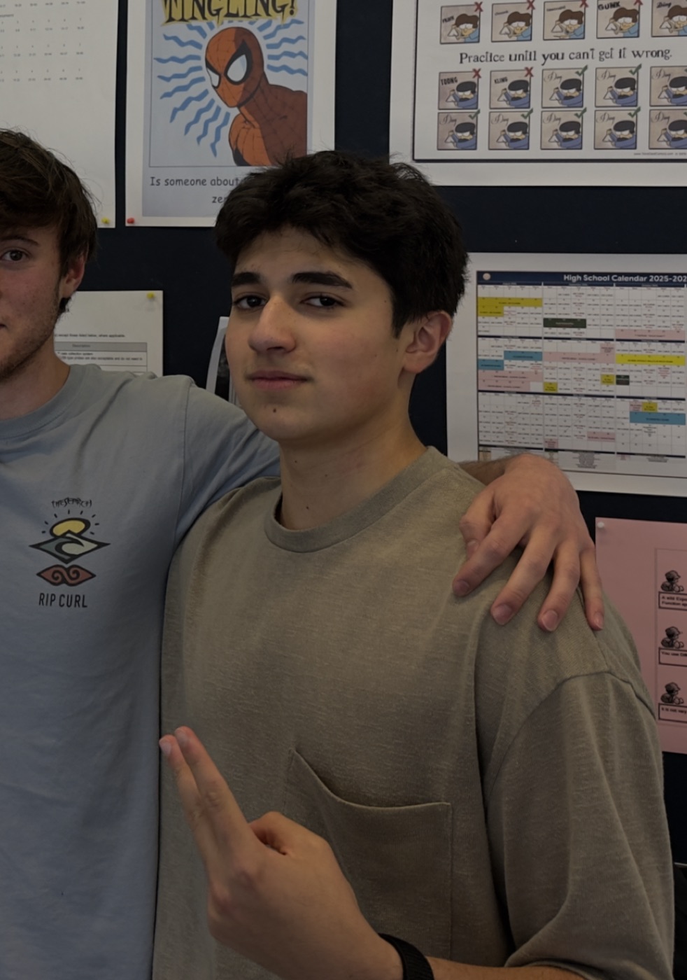 abdullah sultan in a classroom with a friend, holding up a peace sign